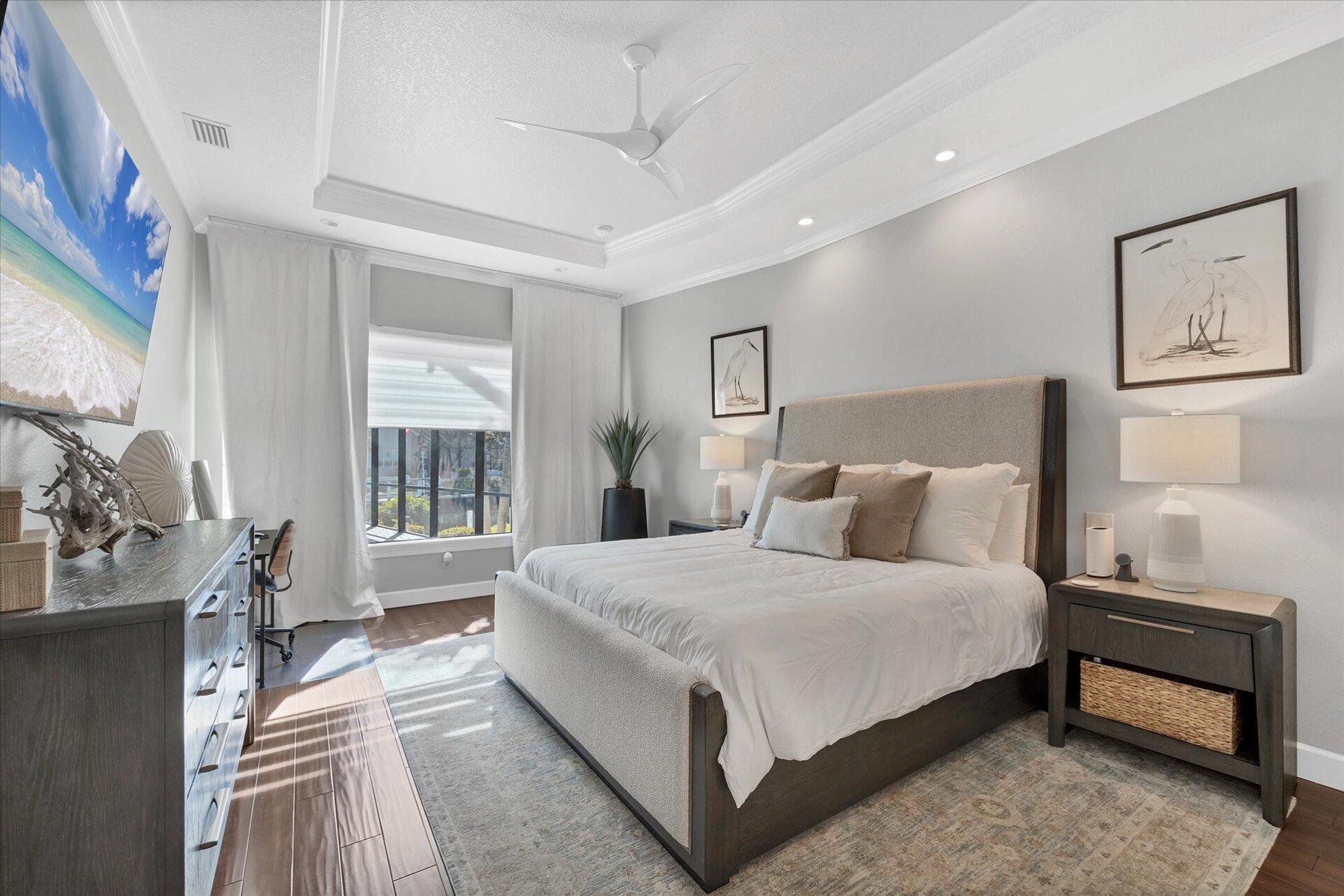 Primary bedroom features king bed, attached bathroom, desk & chair, 65-inch Smart TV, and beautiful view of pool and canal